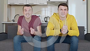 Two men sitting on the couch and watching decisive moment of football match