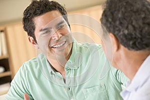 Two men sitting in living room talking and smiling