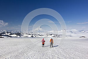 Two men on snowy field in kamchatka mountains near covered by snow volcanoes