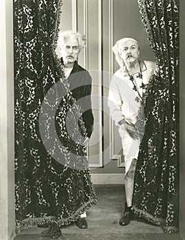 Two men spying from behind drapes