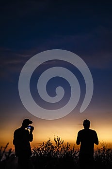 Two men stand with cameras as the sun is setting