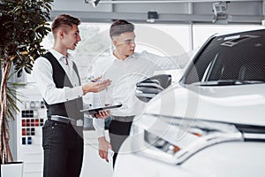 Two men stand in the showroom against cars. Close-up of a sales manager in a suit that sells a car to a customer. The