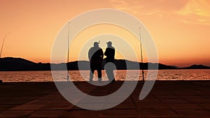 Two men are standing on the quay and fishing in twilight with mountains on background in slowmo