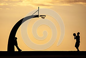 two men standing in silhouette playing basketball against a sunset sky
