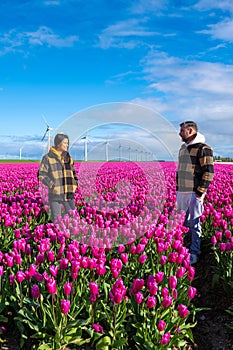 Two men standing tall in a sea of vibrant purple tulips, surrounded by windmill turbines in the Dutch countryside during