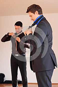 Two men in suits tie their ties