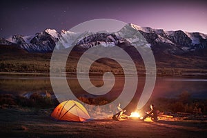 Two men tourists sitting at the illuminated tent near campfire