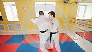 Two men training their aikido skills. A man grabs his opponent and throws him over
