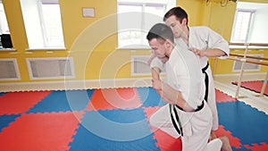 Two men training their aikido skills in the studio. A man grabs his opponent and throws him on the floor