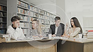 Two men and two women college students laughing while preparing for exams while sitting at table at university library