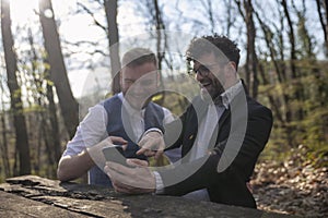 Two men, using smartphone in forest. Selective focus on foreground smartphone, two men out of focus