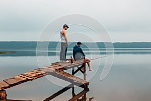 Two men are waiting on a wooden bridge when the fish are biting.