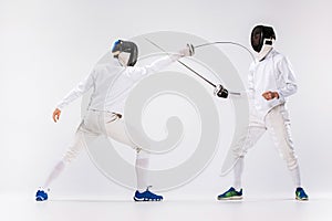 The two men wearing fencing suit practicing with sword against gray