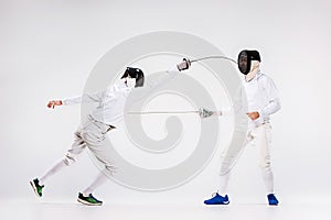 The two men wearing fencing suit practicing with sword against gray