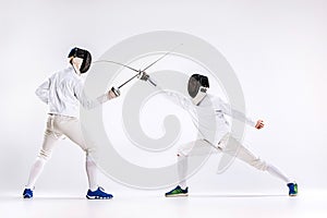 The two men wearing fencing suit practicing with sword against gray