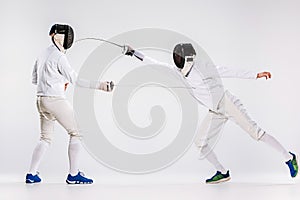 The two men wearing fencing suit practicing with sword against gray