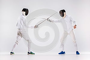 The two men wearing fencing suit practicing with sword against gray