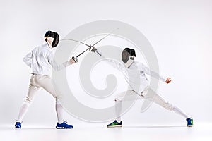 The two men wearing fencing suit practicing with sword against gray photo