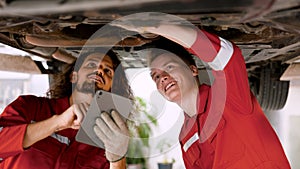 two men who are mechanics, working in large garage, two mechanics checking undercarriage car raised high see lower part clearly,