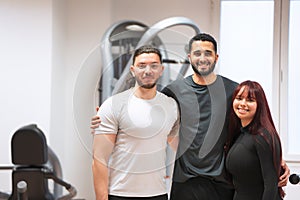 Two men and a woman pose together, smiling in the gym.