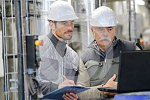 Two men working with laptop in factory