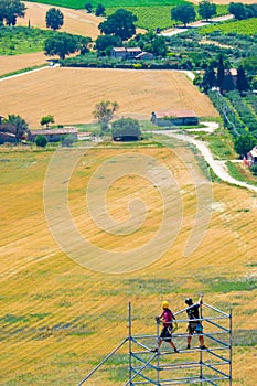 Two men are working on a scaffold, on background the italian countryside from city of Assisi, Italy, in a summer sunny day