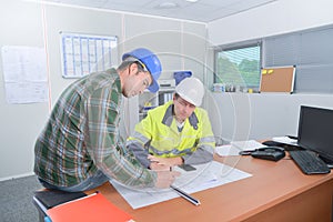 Two men working on scale drawings one sat on table