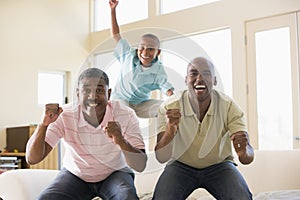 Two men and young boy in living room cheering