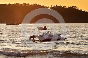 Two mens at sunset pull hydrocycle out of the water. Summer vacation. Water bike loaded onto a trailer
