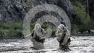 Two mercenary soldiers ford a river during a sabotage operation.