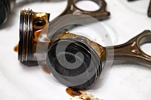 Two metal car pistons in poor condition with soot oil removed from used engine in a deposit of oil lying on workbench in a vehicle