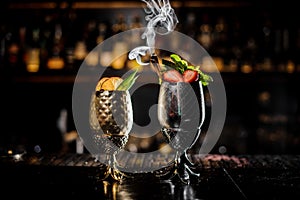 Two metal glasses of fresh summer cocktails decorated with fruit on the bar counter