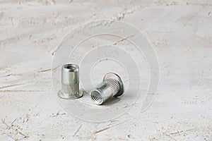 Two metal grey river nuts for hard internal thread for thin units on left part of oblong horizontal shot textured cement