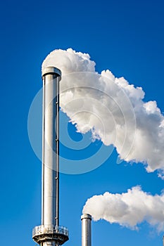 Two metallic chimneys spitting out white smoke against blue sky