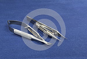 Two microsurgical instruments on blue background
