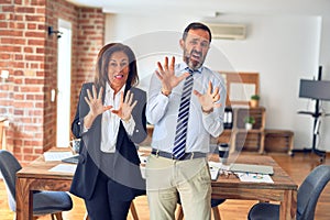 Two middle age business workers standing working together in a meeting at the office afraid and terrified with fear expression