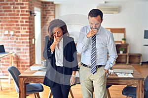 Two middle age business workers standing working together in a meeting at the office feeling unwell and coughing as symptom for