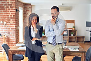 Two middle age business workers standing working together in a meeting at the office looking confident at the camera smiling with