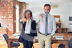 Two middle age business workers standing working together in a meeting at the office looking unhappy and angry showing rejection