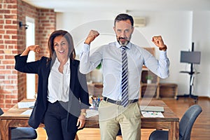 Two middle age business workers standing working together in a meeting at the office showing arms muscles smiling proud