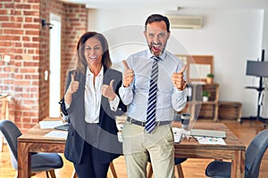 Two middle age business workers standing working together in a meeting at the office success sign doing positive gesture with