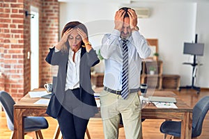 Two middle age business workers standing working together in a meeting at the office suffering from headache desperate and