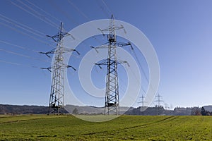 two mighty power poles on a green meadow in front of a cloudless blue sky in sunshine  in the daytime without people