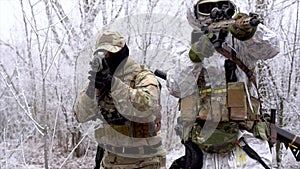 Two military men in white camouflage and green uniform, in winter forest. Soldiers with machinegun sneaking up alonge road, front