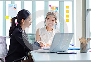 Two millennial Asian young beautiful professional successful businesswoman colleagues sitting smiling in meeting room having funny