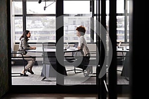 Two millennial businesswomen meeting for a job interview, full length, seen through glass wall