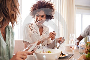 Two millennial girlfriends talking at the table and serving food during lunch with friends, close up