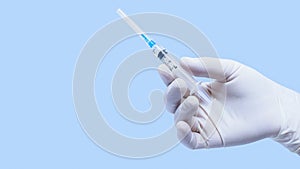 a two-milliliter syringe with 0.5 ml of liquid for injection in a hand in a rubber glove on a blue background. Vaccine test