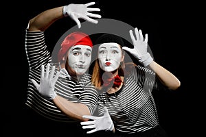 Two mimes leaning on imaginary wall with hands in white gloves