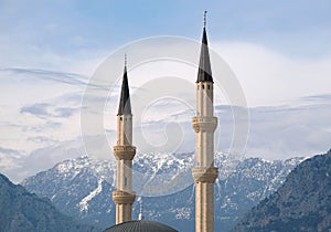 Two minarets rise against the backdrop of impregnable snow-capped mountains covered with trees under serene blue sky